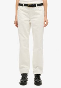 Jeans blancos de algodón con corte recto, que cuentan con cinco bolsillos y herrajes de metal, combinados con un cinturón negro y botas de combate negras.
