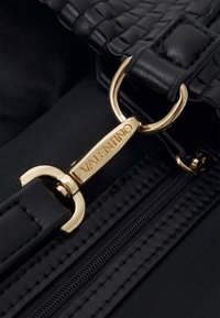 Black woven leather handbag strap with a gold-tone metallic clasp featuring "Valentino" engraved, alongside a black fabric zipper.