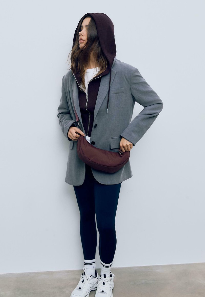 Šedý blazer cez fialovú mikinu, skombinovaný s námorníckymi legínami, bielymi teniskami a hnedou crossbody kabelkou. Oblečenie sa vyznačuje vrstvenými textúrami.