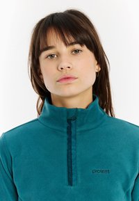 Fleece pullover in teal met een half-rits aan de voorkant, staande kraag en zwart logo-detail. Zachte textuur, casual ontwerp, lichtgewicht stof.