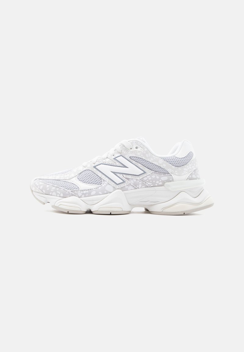 Λευκό και ανοιχτό γκρι αθλητικό παπούτσι New Balance με πάνελ από δίχτυ, πουά σχέδιο και χοντρή σόλα, εμφανιζόμενο από το πλάι σε απλό φόντο.