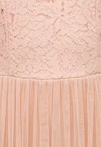 Ήπιο ροζ ύφασμα φόρεμα με λουλουδάτο δαντελένιο σχέδιο στο πάνω μέρος και πλισέ τούλινη φούστα από κάτω.