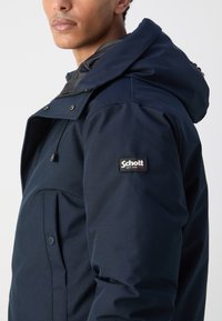 Navy blue hooded jacket with a smooth texture, featuring snap closures, a front pocket, and a branded patch on the left arm.
