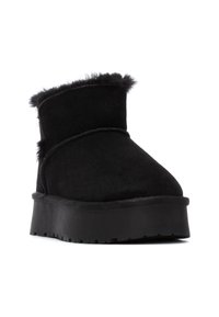 Botín negro con parte superior de imitación ante, forro de piel de peluche en la parte superior y suela negra gruesa y texturizada para una mejor tracción.