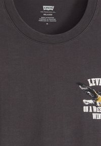 Sötét szürke pamut póló, kerek nyakkal, laza szabással, elöl egy sas grafikával és a "LEVI'S ON A WEST WIND" felirattal.