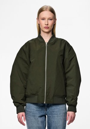 Giacca bomber verde oliva con zip frontale, polsini a coste e vestibilità oversize. Presenta due tasche laterali. Indossata sopra un denim casual.