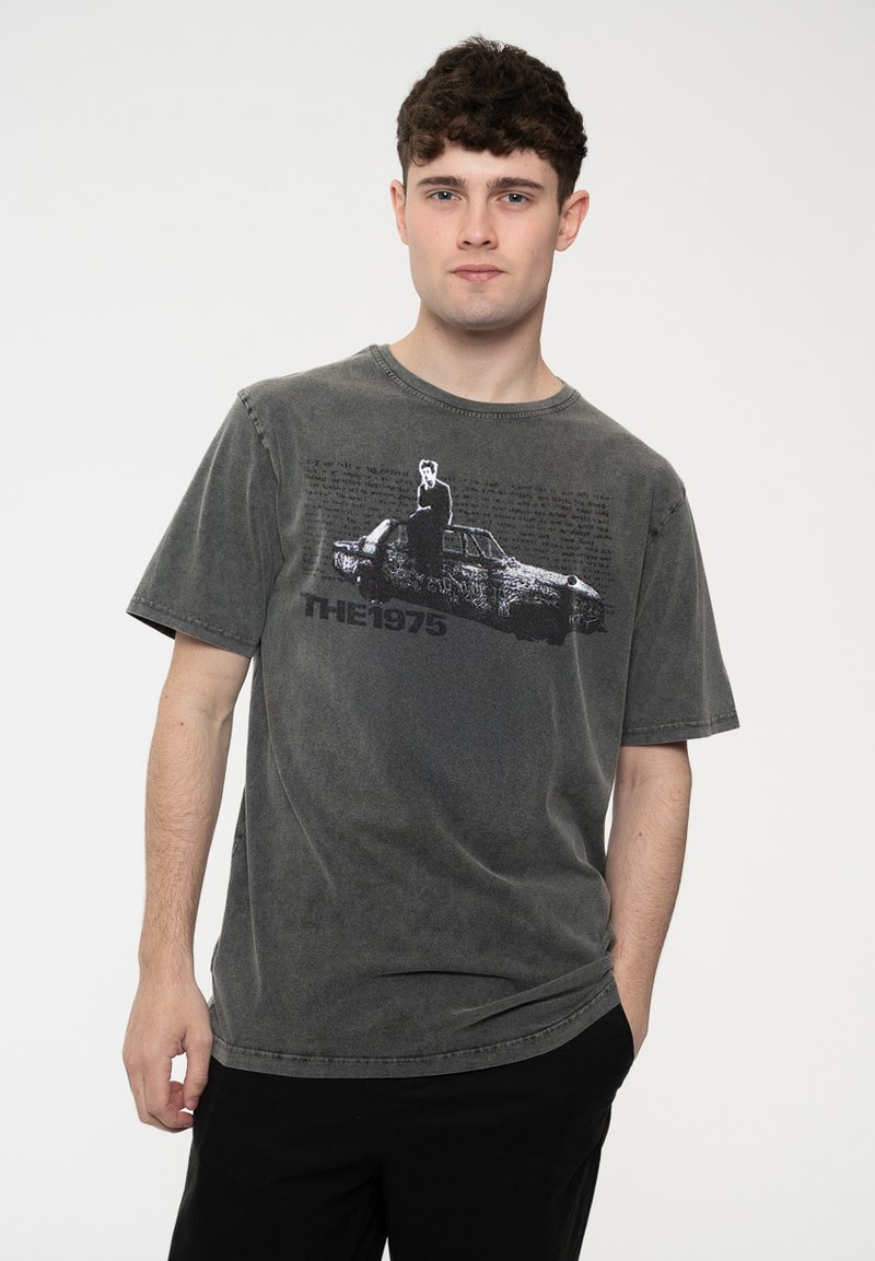 Gray oversized t-shirt with a round neckline. Features a graphic of a car and text reading "THE 1975" printed in black. Soft, textured fabric.