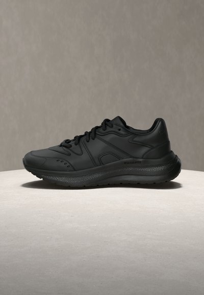 Μαύρο αθλητικό παπούτσι με λείο συνθετικό επάνω μέρος, μαλακή σόλα και υφή στις πλευρές. Περιλαμβάνει κορδόνια και λεπτομέρειες αερισμού.