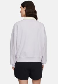 Jasnofioletowy sweatshirt o luźnym kroju, z długimi rękawami i żebrowanym dołem, zestawiony z czarnymi szortami, widoczny z tyłu.