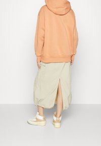 Orange hoodie, beige midikjol med slits bak, och vita sneakers med beige detaljer. Avslappnad, ledig outfit.