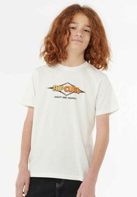 Weißes Baumwoll-T-Shirt mit einem grafischen Logo in Orange und Schwarz, kurzer Ärmel und klassischer Schnitt. Schwarze Hose vervollständigt das Outfit.