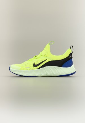 Heldere gele sportschoen met zwarte en blauwe accenten, witte dikke zool, Nike-logo aan de zijkant en trek-lussen op de tong en hiel.