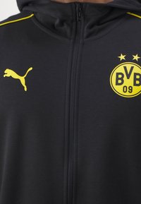 Felpa nera con zip, logo giallo Puma sul lato sinistro del petto ed emblemma del Borussia Dortmund BVB 09 con due stelle sul lato destro del petto.
