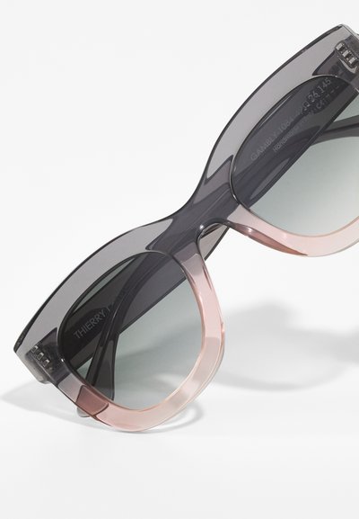 Lunettes de soleil à dégradé noir et rose avec des montures ovales surdimensionnées et des verres sombres. Présente des branches transparentes et un marquage à l'intérieur.