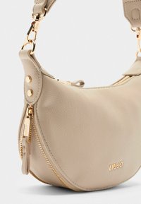 Borsa a spalla in pelle beige con finiture dorate, forma arrotondata e dettaglio con zip. Caratterizzata da stampa del logo e tracolla regolabile.