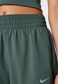 Zöld sportnadrág, könnyű és sima anyagból készült, rugalmas derékpánttal rendelkezik, bal alsó részén pedig egy kis ezüst Nike logó található.