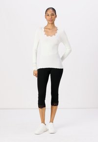 Haut à manches longues blanc à côtes avec un col en dentelle, associé à des leggings capri noirs avec un bord en dentelle à l'ourlet et des baskets blanches.