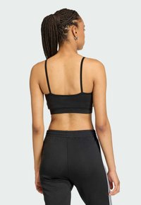 Čierny športový crop top s tenkými ramienkami, spárovaný s čiernymi teplákmi s bielymi bočnými prúžkami, zobrazený zozadu. Hladká tkanina.