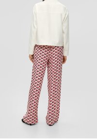 Giacca bianca con colletto; pantaloni rosa con un motivo a freccia ripetuto di un rosa scuro; vestibilità comoda. Tessuto dalla texture liscia in tutto.