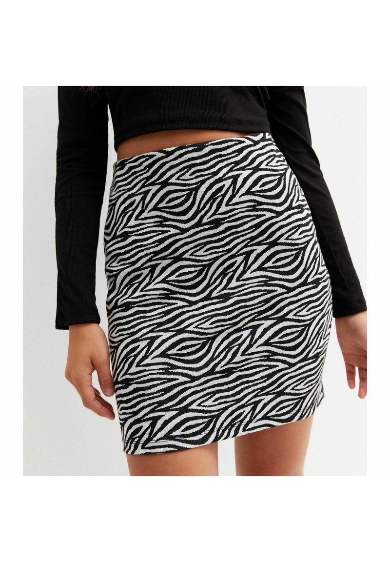 Femme portant un crop top noir à manches longues et une mini-jupe taille haute à imprimé zèbre noir et blanc.