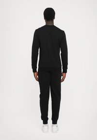 Black sweatshirt and matching joggers in a soft, textured fabric. Features a crew neck, ribbed cuffs, and fitted waistband.