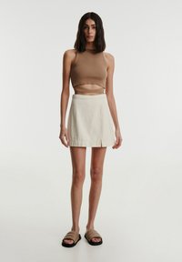 Beige, verkürztes Tanktop mit Ausschnitt, kombiniert mit einem cremefarbenen Minirock und beigen Slipper-Sandalen. Glattes Material, minimalistisches Design.