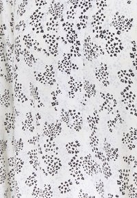 Tessuto bianco con un motivo a macchie nere e grigie, con dettagli sulla tasca. Texture liscia, design leggero.