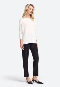 Top crème à manches longues avec texture côtelée, associé à un pantalon noir ajusté et des escarpins noirs à bout pointu avec une touche brillante.