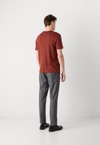 Tricou scurt de culoare ruginie, purtat cu pantaloni gri și pantofi negri. Tricoul are un gât rotund și o croială lejeră.