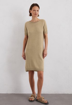 Robe tricotée à manches courtes en beige clair avec un col rond et une coupe décontractée, dotée d'un ourlet côtelé. Associée à des sandales à glissière marron.