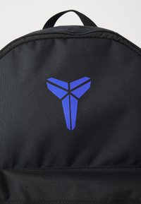 Zwarte rugzak met een gestructureerde afwerking, featuring een opvallend blauw logo in de vorm van een gestileerde letter. Voorzien van een handvat aan de bovenkant en een rits.