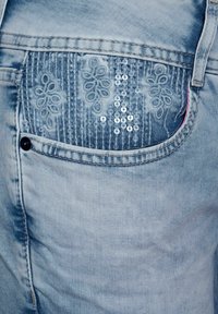 Tascone in denim blu chiaro con ricami floreali e dettagli in paillettes argento verticali.