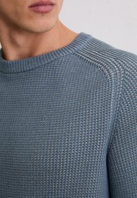 Getextureerde blauwe trui met een geribbelde breipatroon, voorzien van een ronde halslijn en subtiele horizontale stiksels op de schouder.