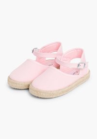 Rožinės drobės espadrilės su kryžminiais diržais ir metalinėmis sagtimis, pasižyminčios pintu džuto padu ir lygiu paviršiumi.