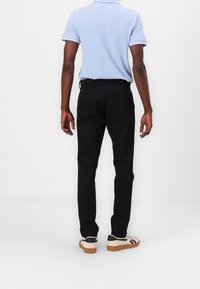 Pantalon noir slim en tissu durable, doté d'un design classique à cinq poches, associé à un polo bleu clair.