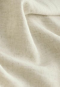 Lys beige linned stof med en let struktureret overflade, der har bløde folder, som skaber et naturligt fald.