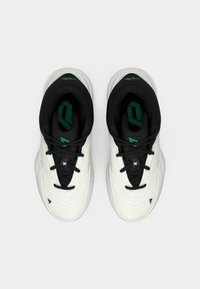 Par bijelih i crnih sportskih tenisica s zelenim ulošcima, gledano odozgo na neutralnoj svijetloj pozadini.