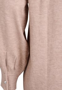 Beżowy sweter z dzianiny z rękawami, które mają okrągłe mankiety ozdobione srebrnym guzikiem. Miękka tekstura, lekko luźny krój i delikatne fałdy.