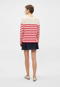 Sarkans un balts svītrots krekls garām piedurknēm, ar mājīgu piegriezumu, apvienots ar tumšu džinsu svārku un gaišiem plakanajiem apaviem.