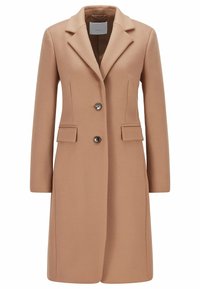 Dameswoljas in kameelkleur met reverskraag, twee knopen, klepzakken en lange mouwen, frontaal getoond op een witte achtergrond.