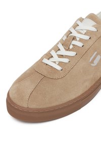 Beežist suede tossud valgestest paeltest, pruuni kummist tallaga ning peene õmbluse detailidega varvaste ja külgede lähedal.