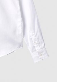 Vit bomullskjorta med långa ärmar, med knappslutna manschetter och en slät, strukturerad textur.