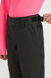 Zwarte broek met een strakke, gladde textuur, voorzien van een brede tailleband en een verstelbare klittenbandsluiting, gecombineerd met een aansluitend roze longsleeve shirt.