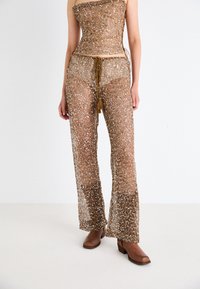 Gold, sequin-covered two-piece outfit: strapless top with a fitted design and loose, wide-leg pants featuring a drawstring. Brown heeled shoes.