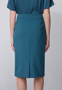 Tealfärgad pennkjol i ett slätt tyg, med en baktill slits, osynlig dragkedja och skräddarsydd design med en subtil lyster.