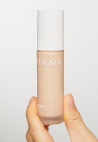 Beige flytande foundation i en klar glasflaska med ett vitt lock. Har präglad text: "LADORA PROMISE LIGHT MATTE." Slät textur.