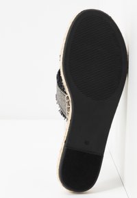 Chaussure slip-on tissée noir et blanc avec une tige en tissu texturé, une semelle intermédiaire en jute, et une semelle en caoutchouc avec un motif strié.