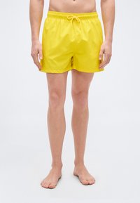 Κίτρινο μαγιό σορτς με ελαστική μέση και ρυθμιζόμενο κορδόνι. Λείο ύφασμα με ελαφριά, γρήγορα στεγνώνουσα υφή. Χωρίς τσέπες.