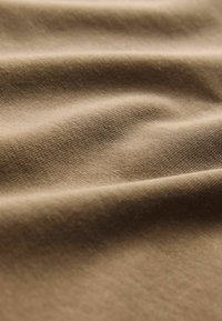 Beiger Stoff mit glatter Textur, der subtile Rillen und Falten aufweist und ein mittleres Gewicht sowie ein weiches, flexibles Material demonstriert.