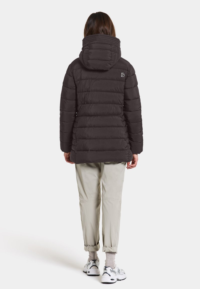 Dunkelgraue Steppjacke mit Kapuze, kastigem Schnitt und horizontaler Steppung. Tragen mit hellen Hosen und Sneakers.